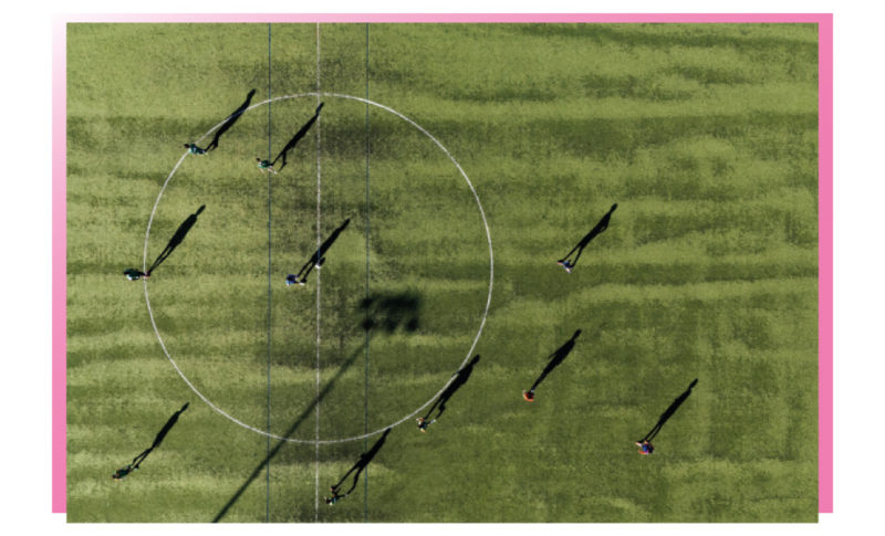 terrain de foot vu du ciel, sur la pelouse verte kaki, une dizaine de personnes se distinguent par leurs ombres